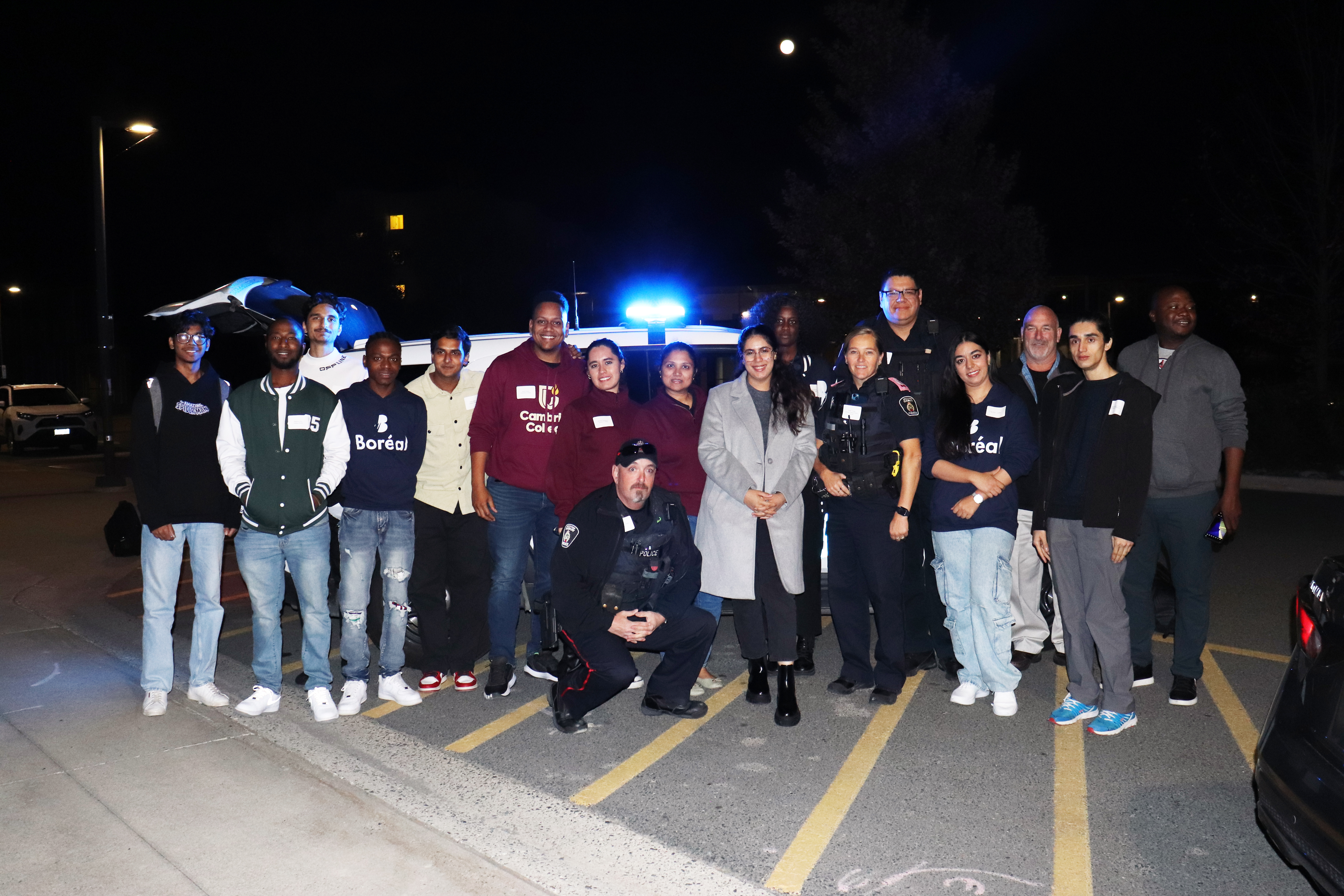 group of people standing outside in front of a cruiser at night